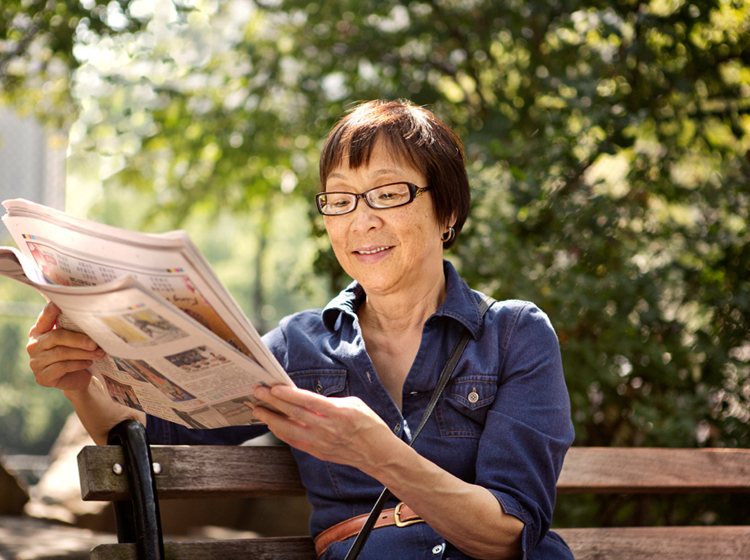 Older woman relaxes and reads newspaper on park bench