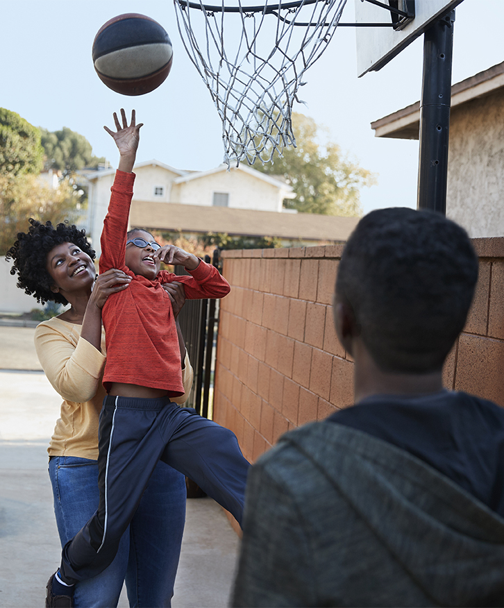 mother plays basketball with her sons in the driveway